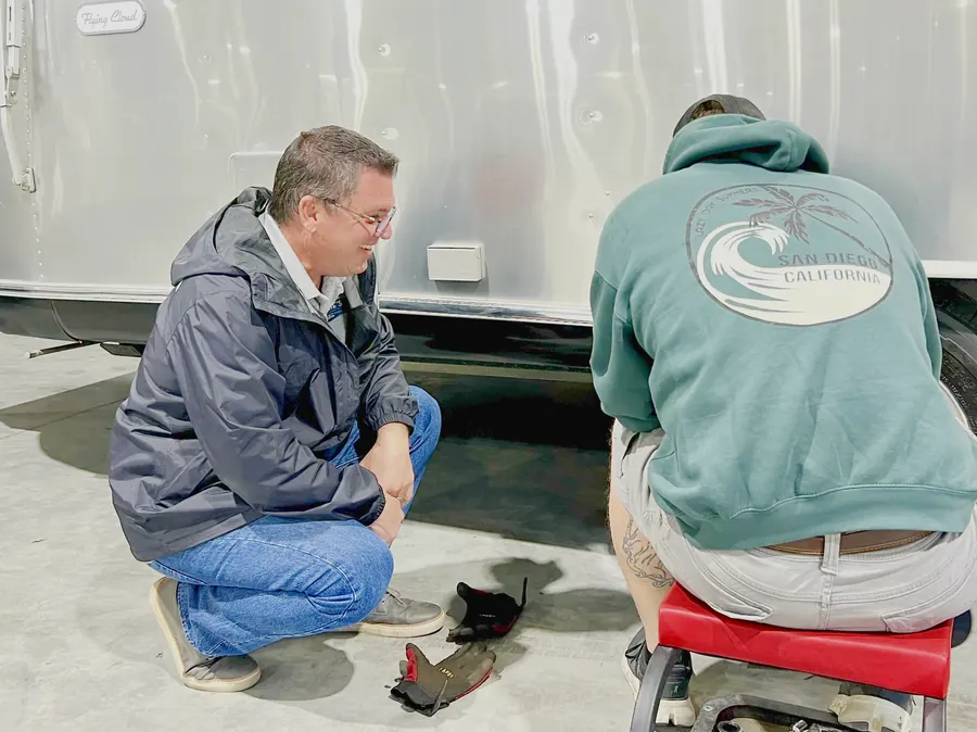 Vinnie Lamica kneeling beside an Airstream with a technician